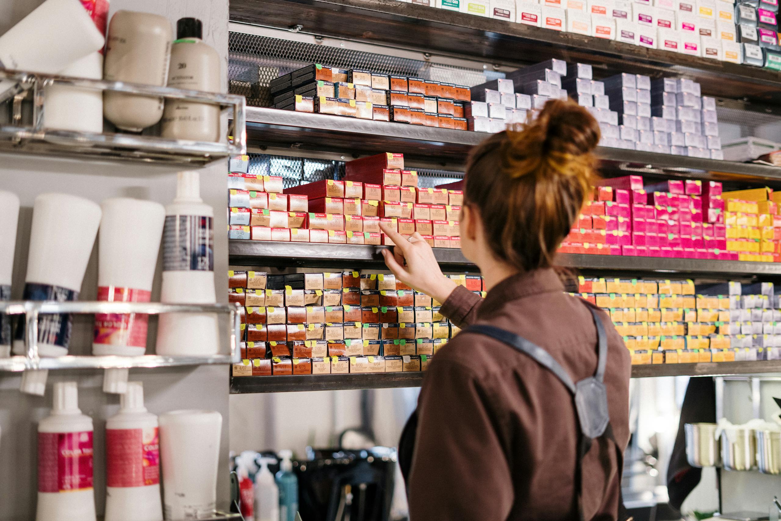 Un coiffeur range des boîtes de couleurs vibrantes sur une étagère dans un salon de beauté.