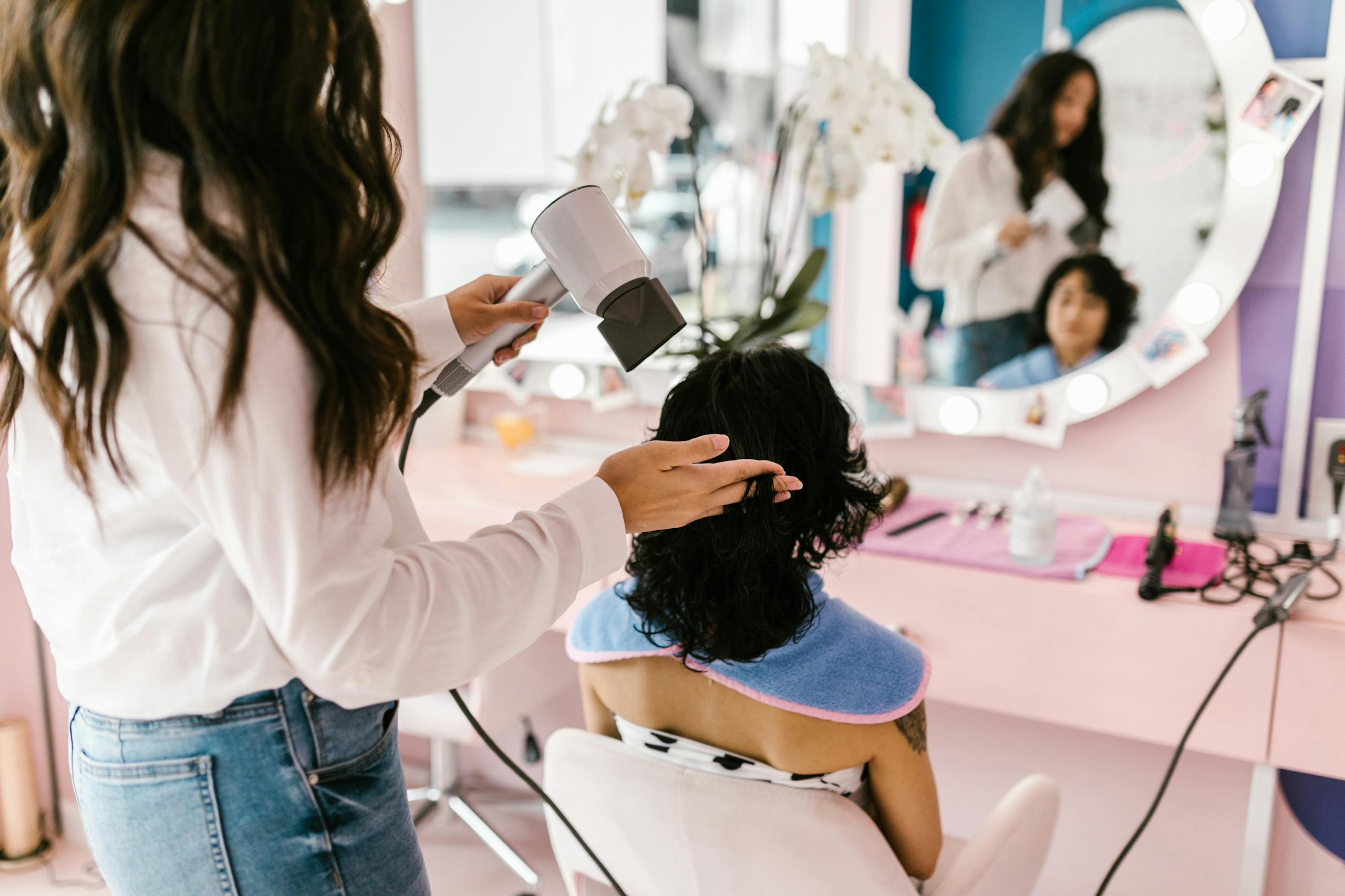 Un coiffeur utilise un sèche-cheveux sur une cliente dans un salon moderne avec un reflet de miroir.
