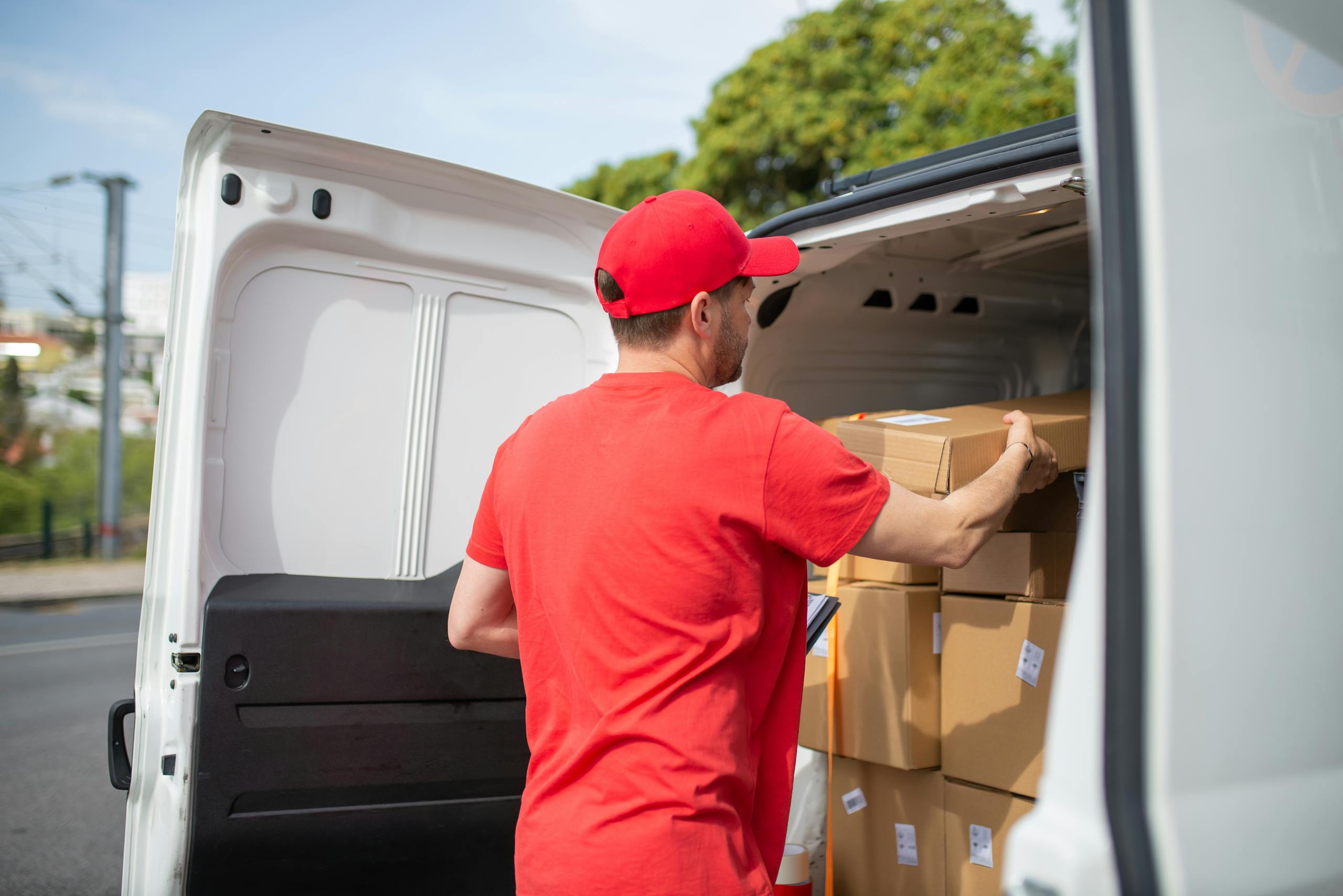 Coursier transportant des paquets dans une camionnette pour les livrer, portant un uniforme rouge.